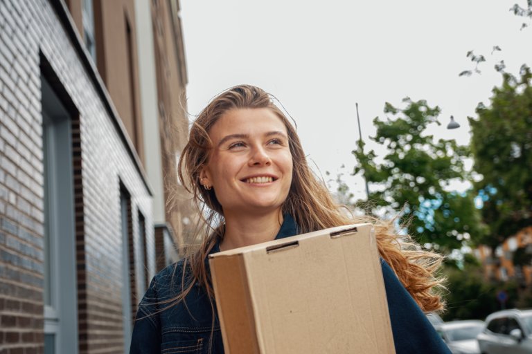 En leende kvinna står med ett paket i handen