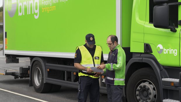 En medarbetare från tull kollar igenom papper från en Bring chaufför som står bredvid en Bring lastbil.
