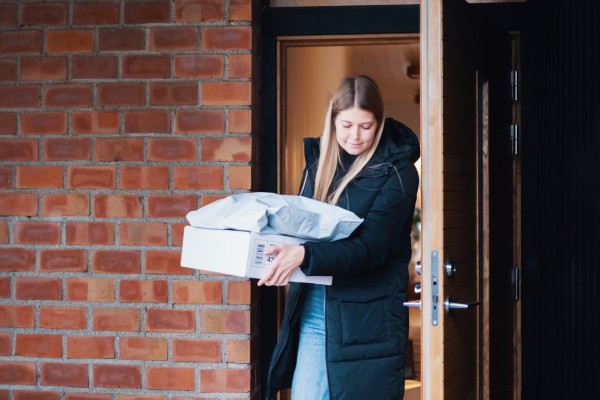 En kvinna går ut genom en ytterdörr med flera paket i handen som ska returneras