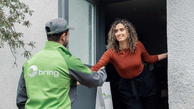 En Bringbud står framför ett hus och lämnar över en leverans till en kvinna som står i dörren