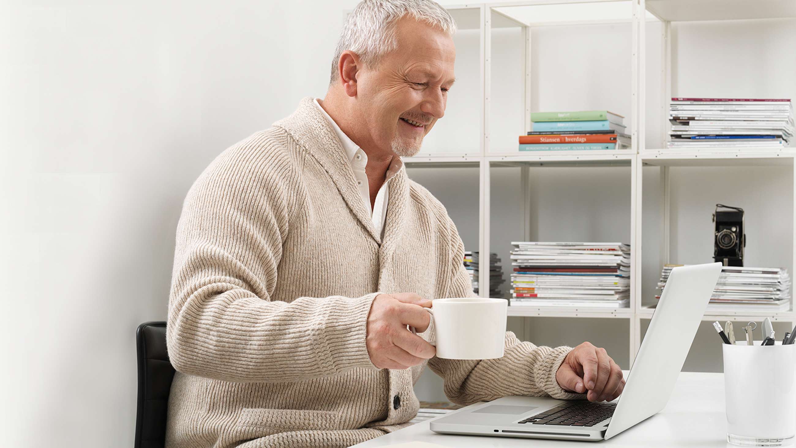 En glad man sitter med en kopp kaffe framför sin dator