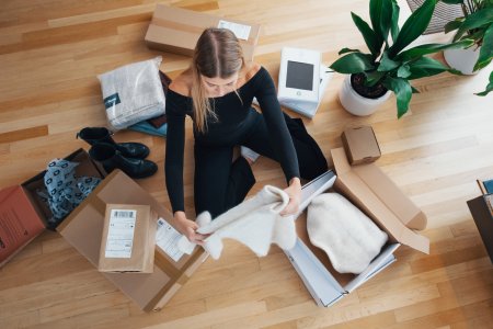 En kvinna sitter på ett paket omgiven av paket med en massa saker i
