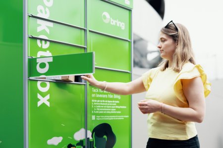 En kvinna står framför en grön Bring-paketbox och returnerar ett paket i en lucka