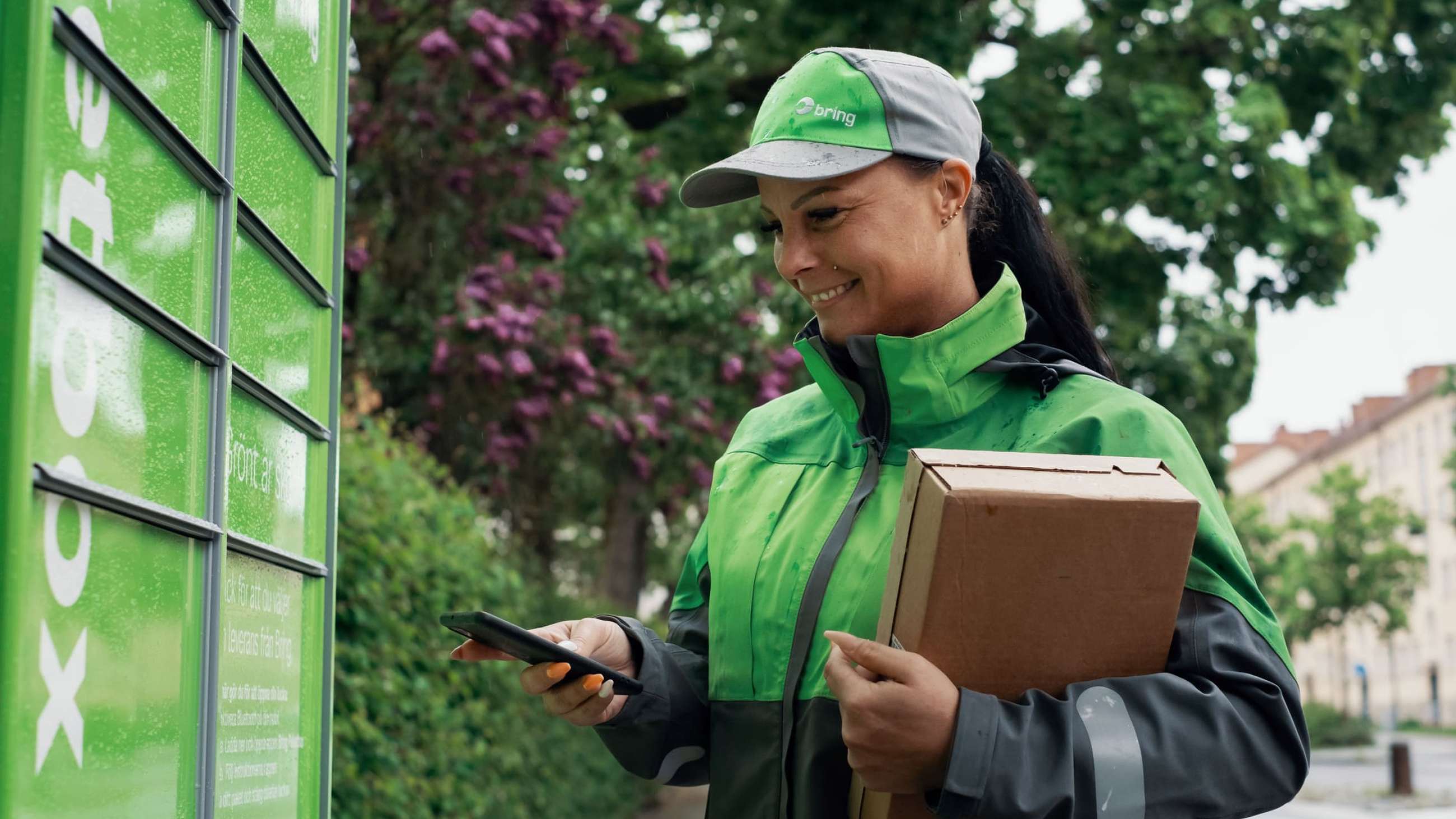 Ett kvinnligt Bringbud levererar ett paket till en paketbox.