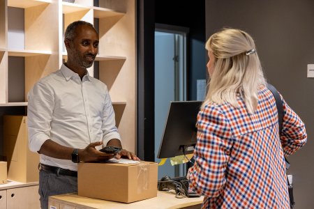 En kvinna returnerar ett paket till en man vid en disk på ett ombud