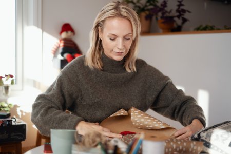 En kvinna sitter vid ett bord och slår in en julklapp.