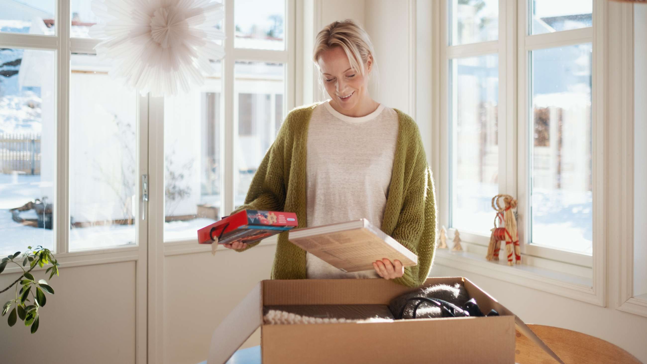 En kvinna står framför ett paket på ett bord med ett spel och en bok i händerna