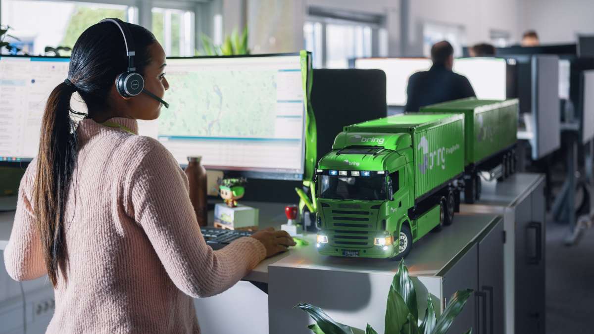 A female coworker at Bring customer service stands in front of a computer with a headset on