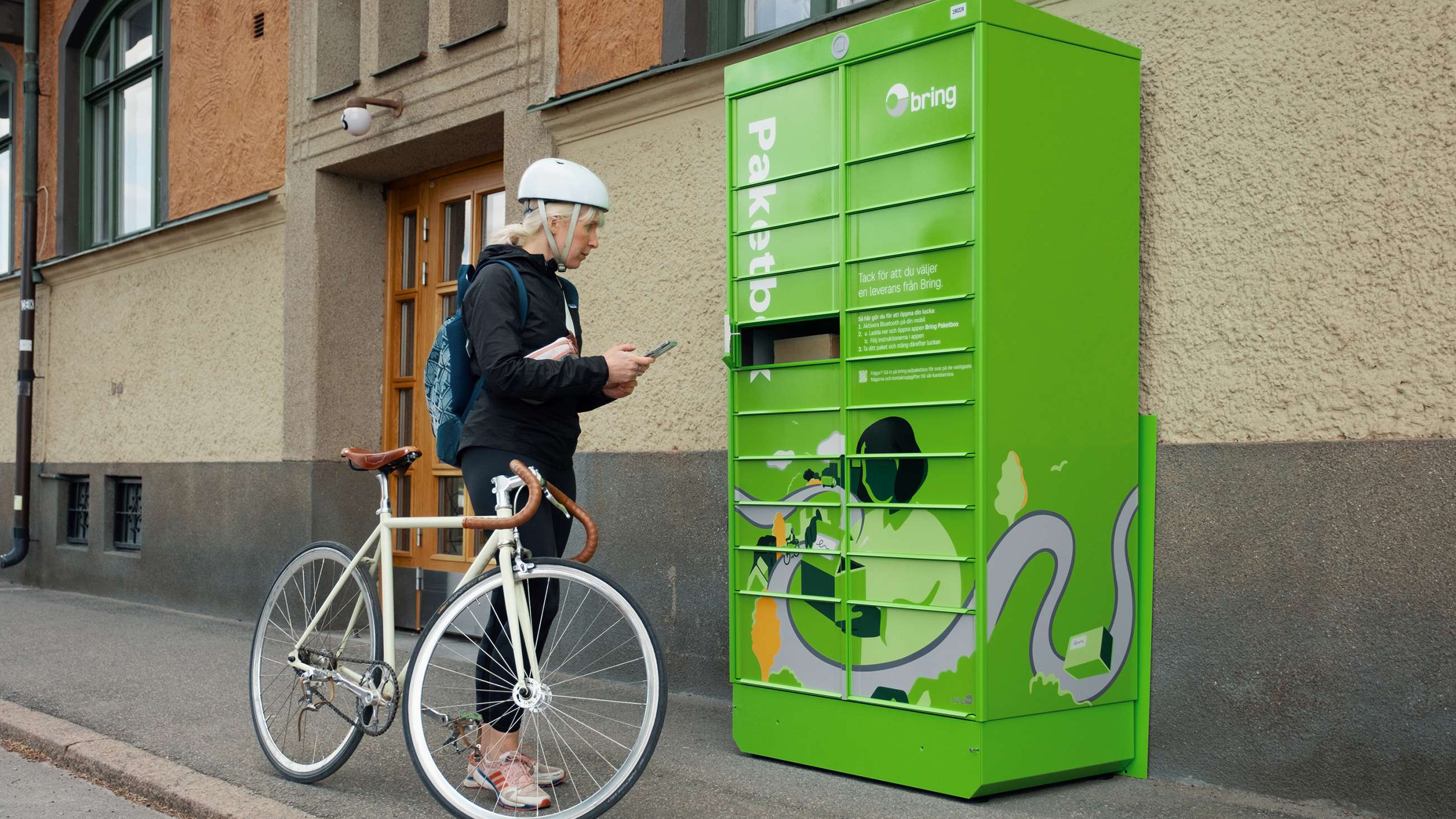 Woman wearing a bicycle helmet picking up parcel in a Bring parcel locker