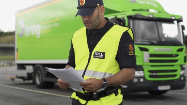 Customs officer checks documents in front of a green delivery van.