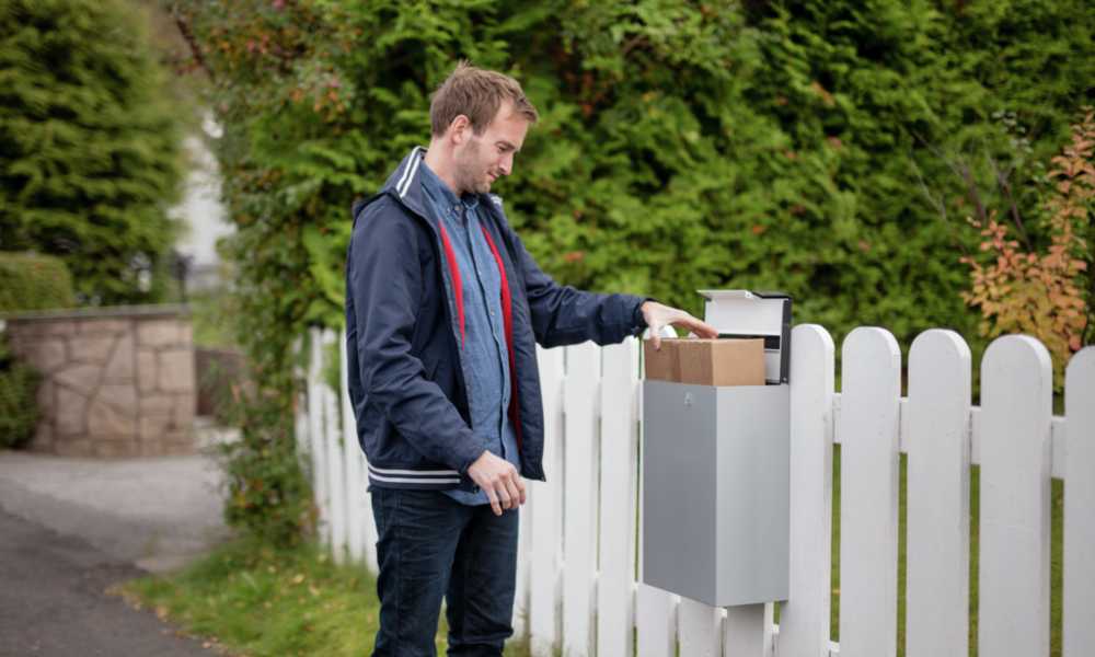 A man is standing in front of a mailbox with a parcel in.