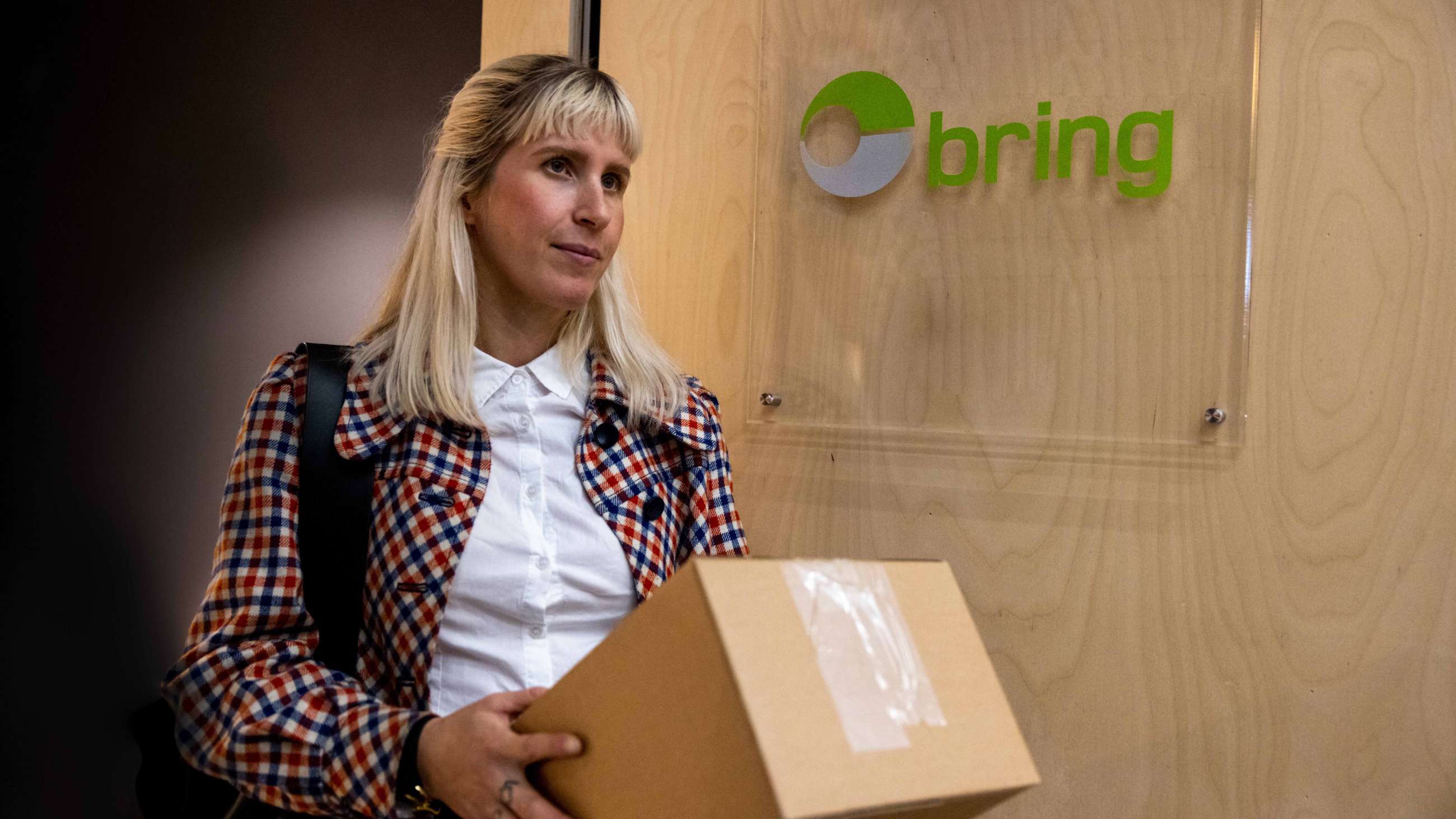 A woman is carrying a box at a Bring pickup point