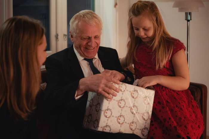 Äldre man sitter med familjen och öppnar sin julklapp.