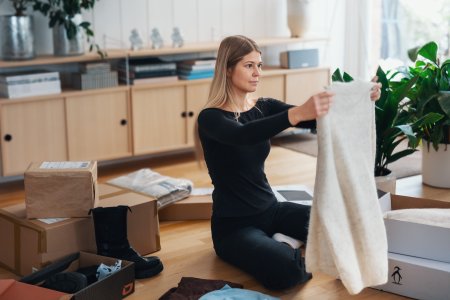En kvinna sitter på knä med flera kartonger runt sig och håller upp en tröja framför sig