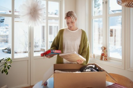 En kvinna står framför ett paket på ett bord med ett spel och en bok i händerna