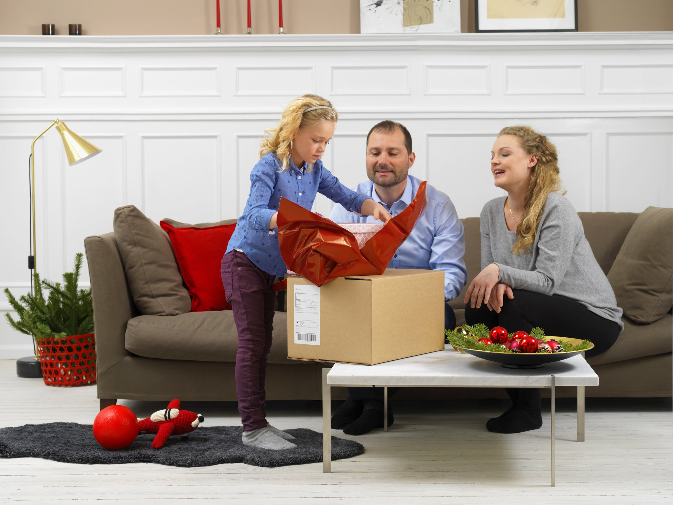 Familj sitter i soffan och öppnar ett paket tillsammans