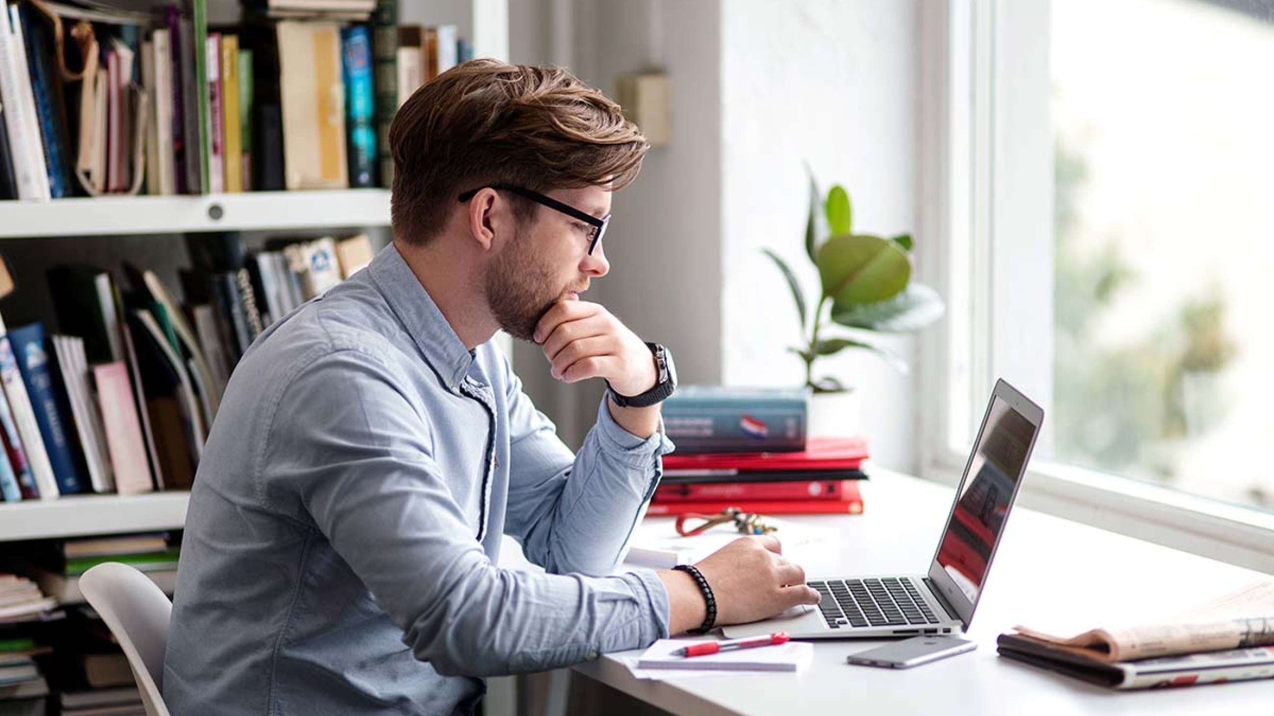 En man iklädd skjorta och glasögon sitter framför en bärbar dator