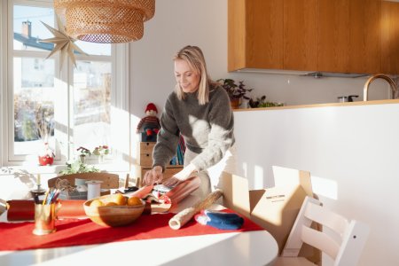 En leende kvinna står lutad över ett bord medan hon slår in en julklapp som hon har handlat på Black Friday