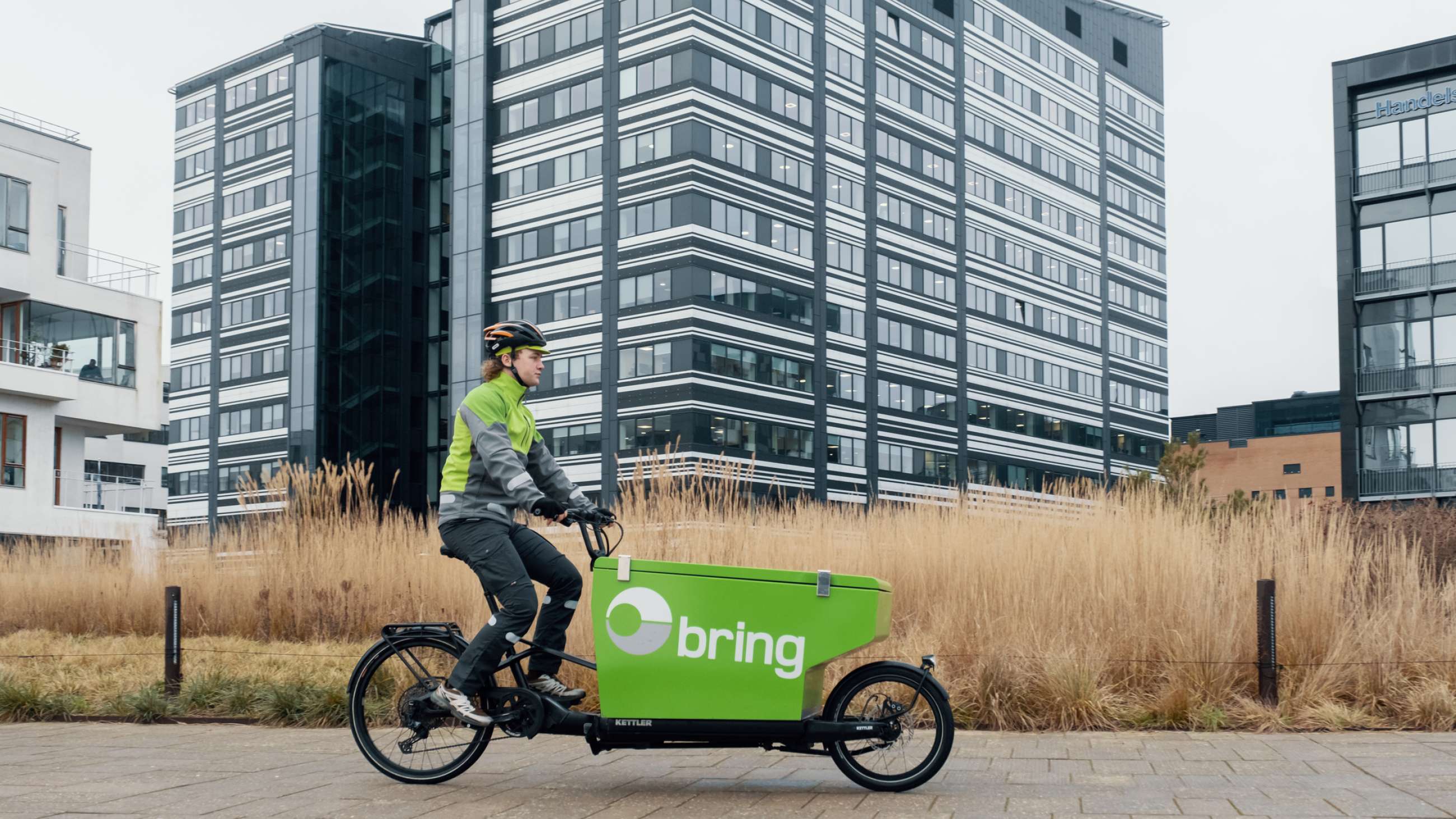 Bringbud på grön elcykel transporterar paket i ett bostadsområde.