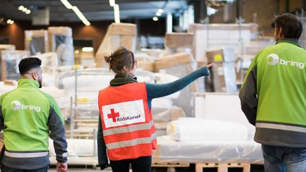 Två Bring medarbetare och en anställd från Röda Korset står på Brings lager med ryggarna mot kameran