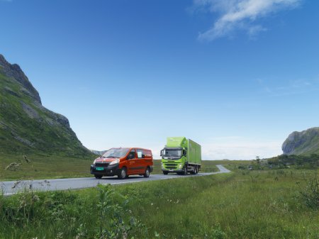 En röd Posten Norge-bil och en grön Bring-lastbil är ute och kör på landsbygden