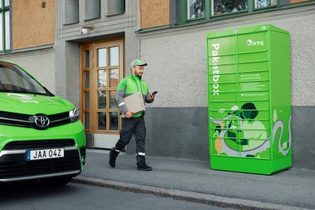 En manlig Bring-chaufför går med ett paket mot en grön Bring-paketbox