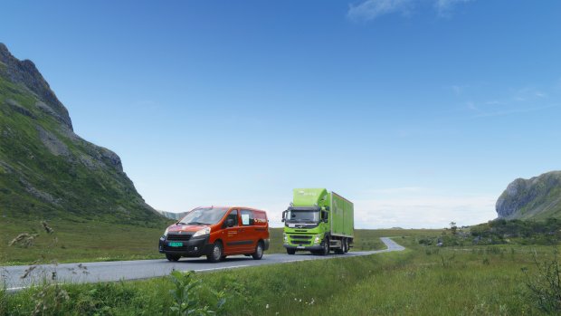 En röd Posten Norge-bil och en grön Bring-lastbil är ute och kör på landsbygden
