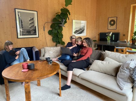 Familj i ett vardagsrum sitter tillsammans med laptop.