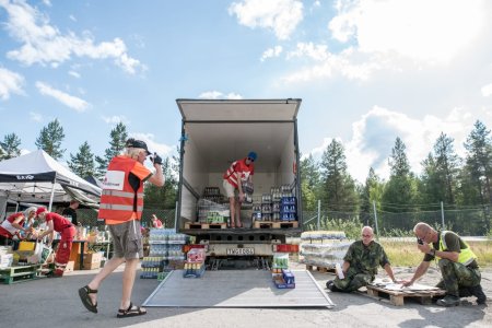 En lastbil öppen baktill med personer från Röda Korset som lastar av paket med dryck från lastbilen