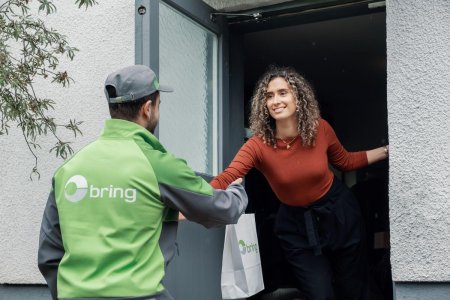 Ett manligt Bring-bud lämnar över en Bring-påse i dörröppningen till en kvinna