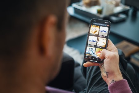 En man sitter och kollar på en webbutik som säljer skor på sin mobil som han håller i handen