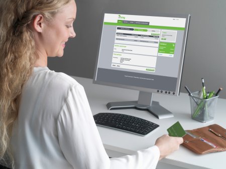 En kvinna sitter vid ett skrivbord framför en dator med ett kreditkort i handen