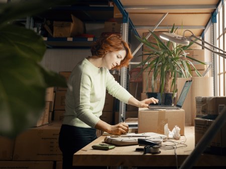 En kvinna står på ett lager med en laptop stående på ett paket framför sig