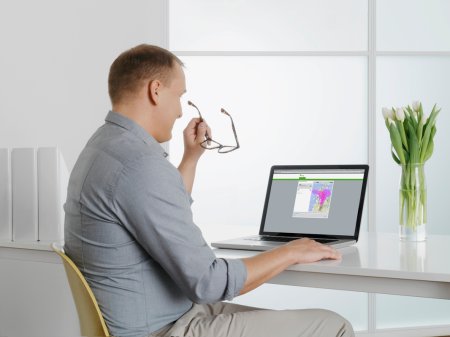 En man sitter vid ett skrivbord framför en dator med ett par glasögon i handen