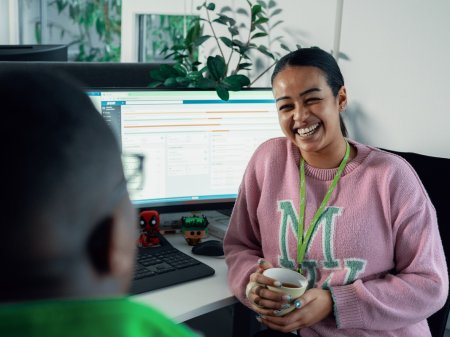 En kvinnlig Bring-medarbetare sitter på kontoret framför en dataskärm och skrattar i samtal med en kollega