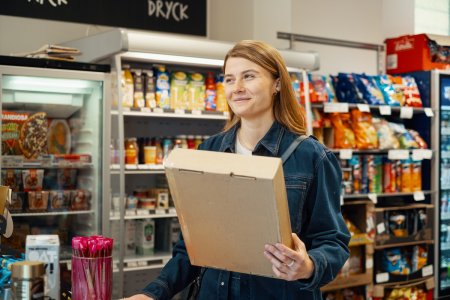 En kvinna står med ett paket i handen inne på ett paketombud