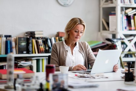 En kvinna sitter på ett hemmakontor framför en laptop