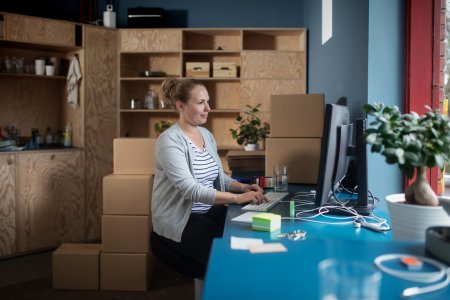 En kvinna sitter vid ett skrivbord framför en dator i ett rum med flera paket staplade på varandra