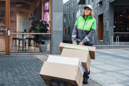 Ett kvinnlig Bring-bud står i stan med en pirra med flera paket på