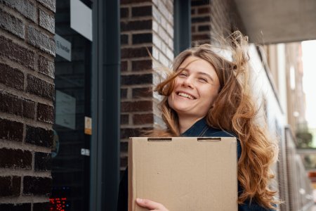 En leende kvinna står framför ett ombud med ett paket i handen