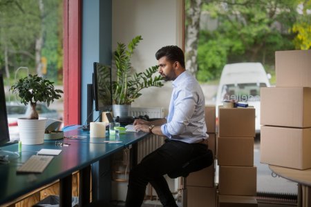 En man sitter vid ett skrivbord framför en dator och i rummet syns flera paket staplade på varandra