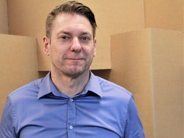 Marcus Eklund, försäljningschef på RAJA, står framför kartonger iklädd en blå skjorta