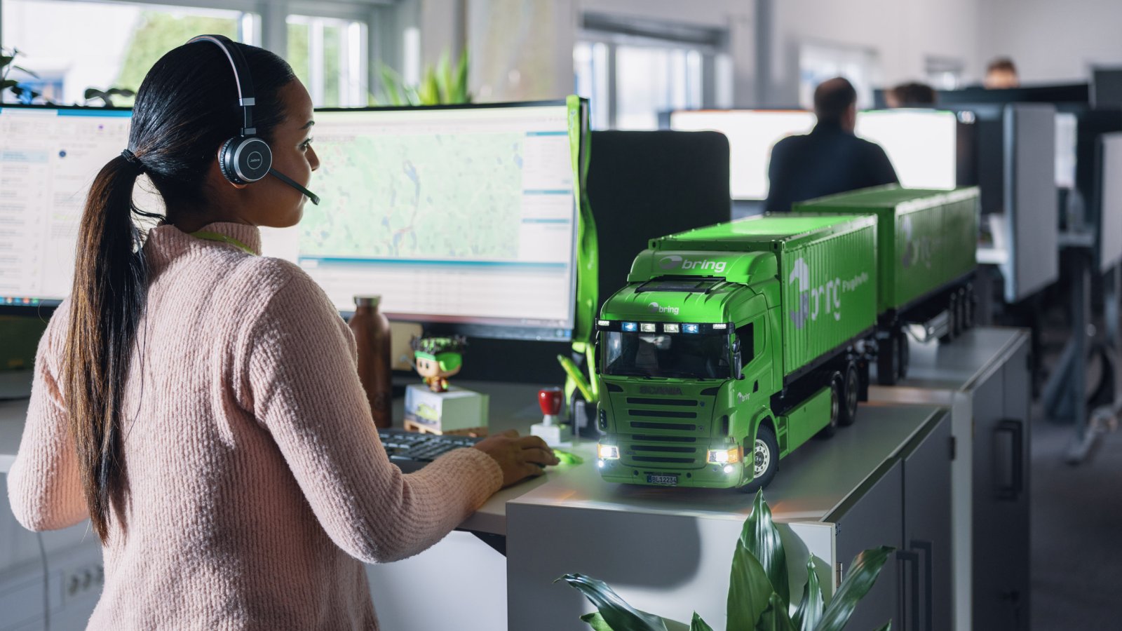 En kvinnlig medarbetare på kundservice står framför en dataskärm med ett headset på huvudet