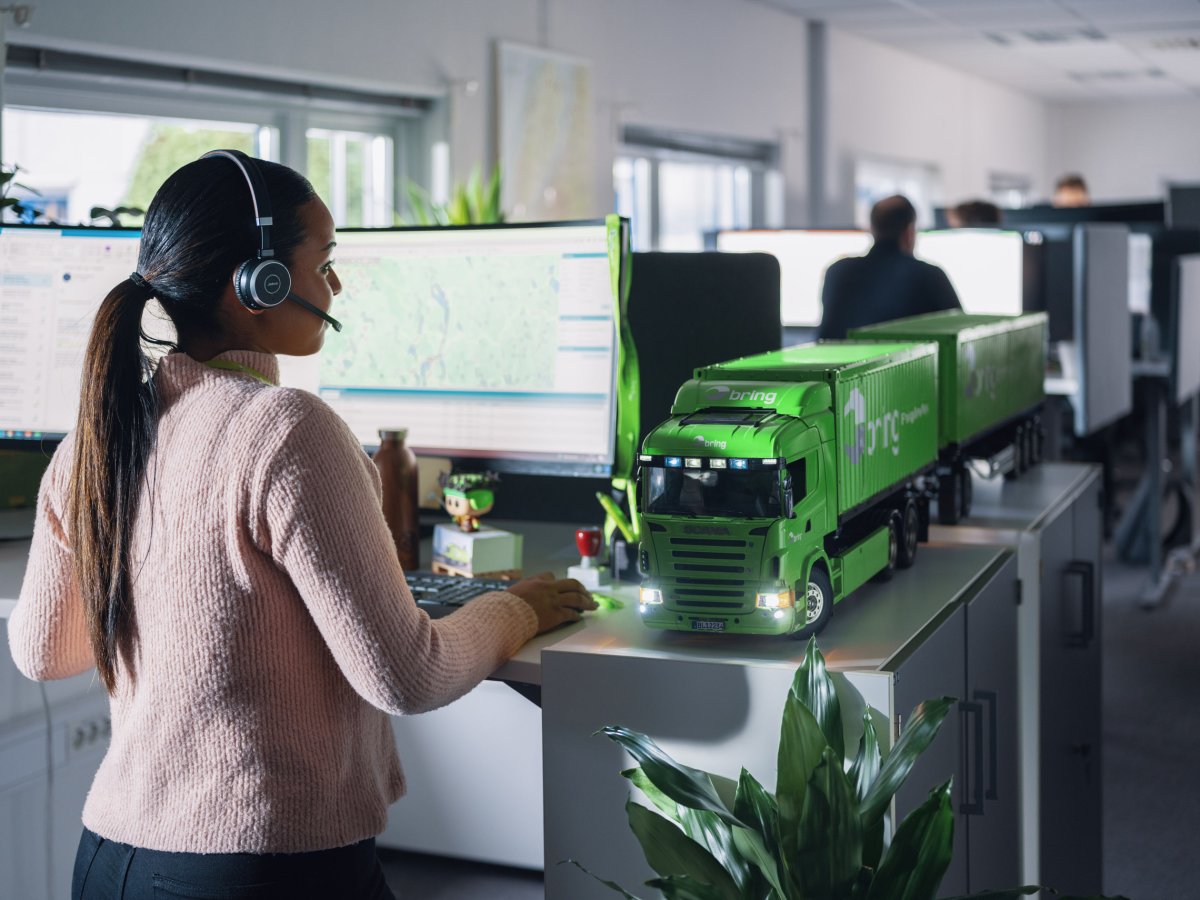 En kvinnlig medarbetare på kundservice står framför en dataskärm med ett headset på huvudet