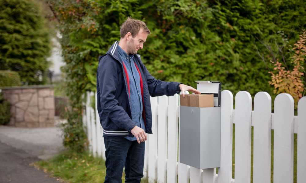 Man står framför en brevlåda med ett paket i.
