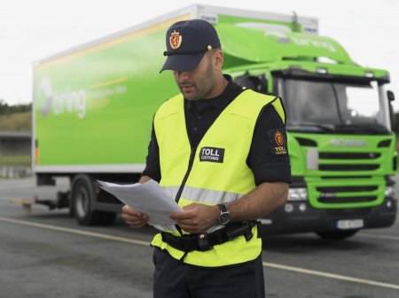 En man som arbetar på tullen står vid en Bring lastbil och kollar igenom några papper